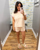 A woman takes a mirror selfie in a fitting room wearing a matching short-sleeve striped pajama set with pink and white horizontal stripes, paired with beige double-strap sandals.