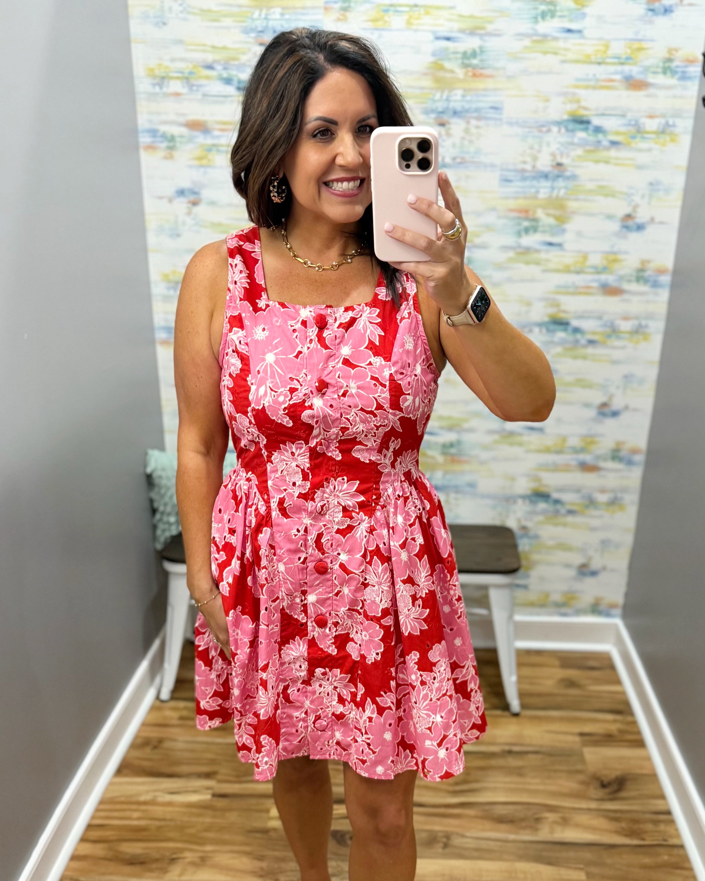 Woman taking a mirror selfie wearing a red floral dress in a room with a colorful wall.