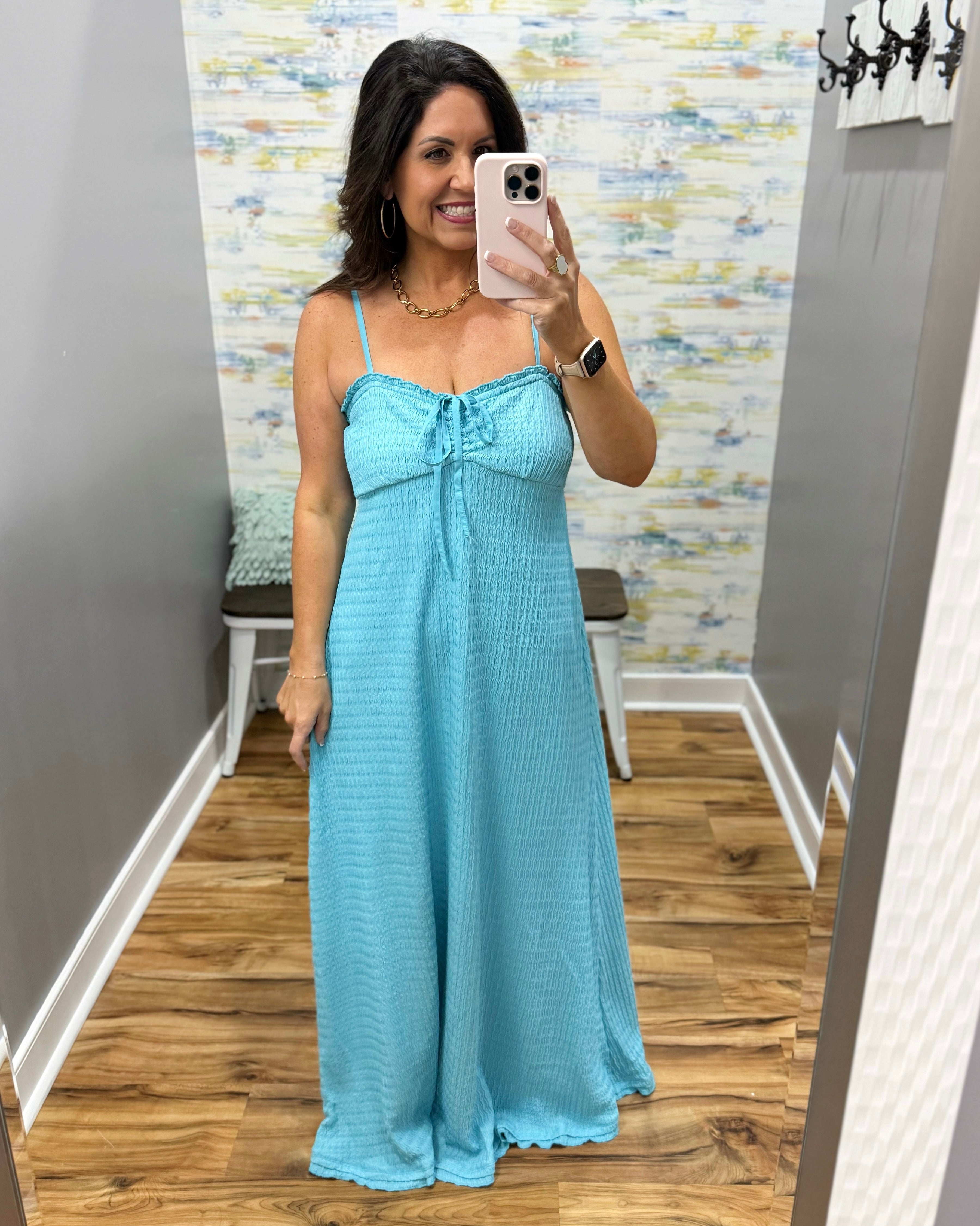 Woman wearing a light blue dress taking a mirror selfie in a room with a patterned wall.