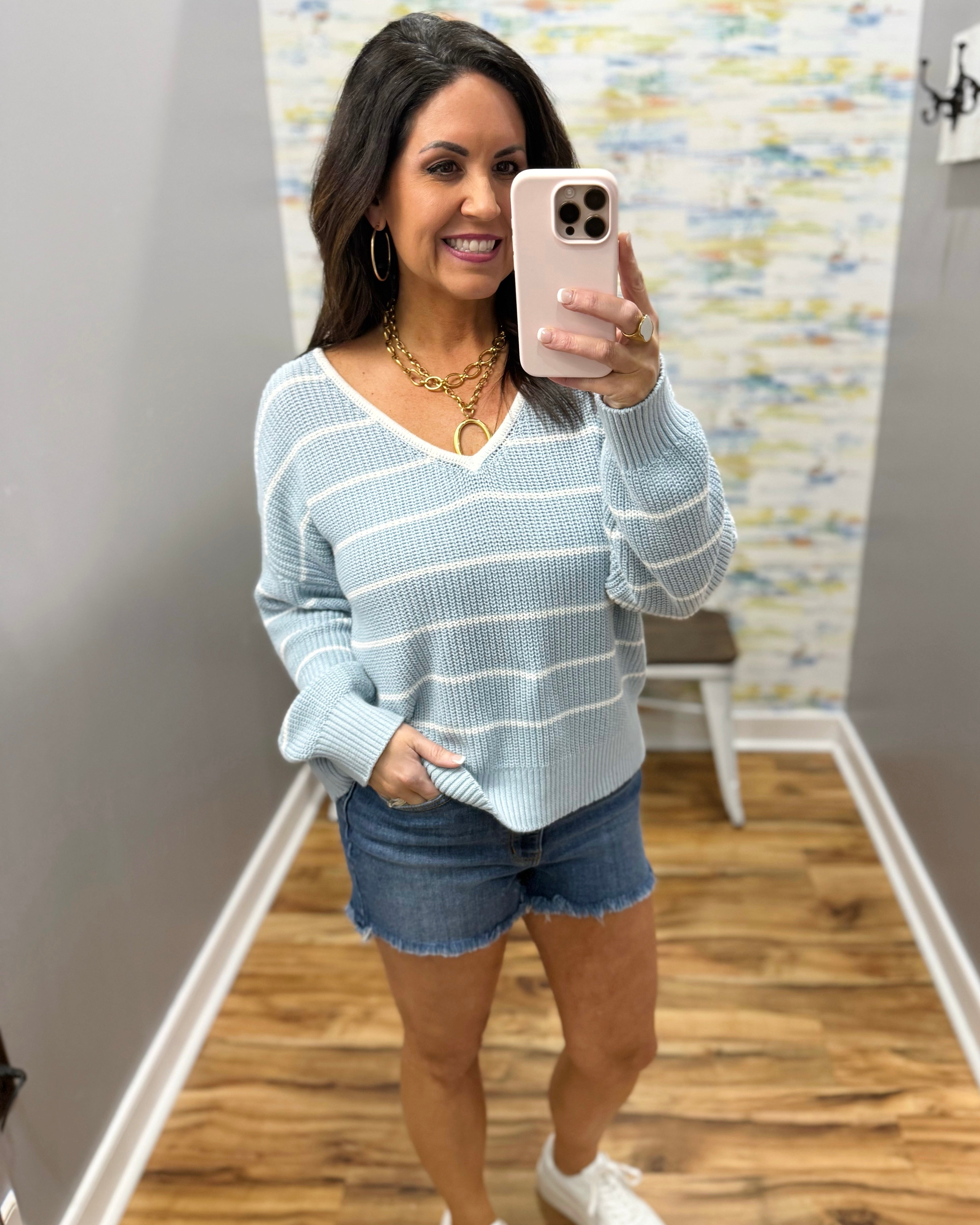 Woman wearing a light blue striped sweater and denim shorts.