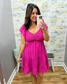 Woman wearing a pink dress taking a mirror selfie in a room with a colorful wall.