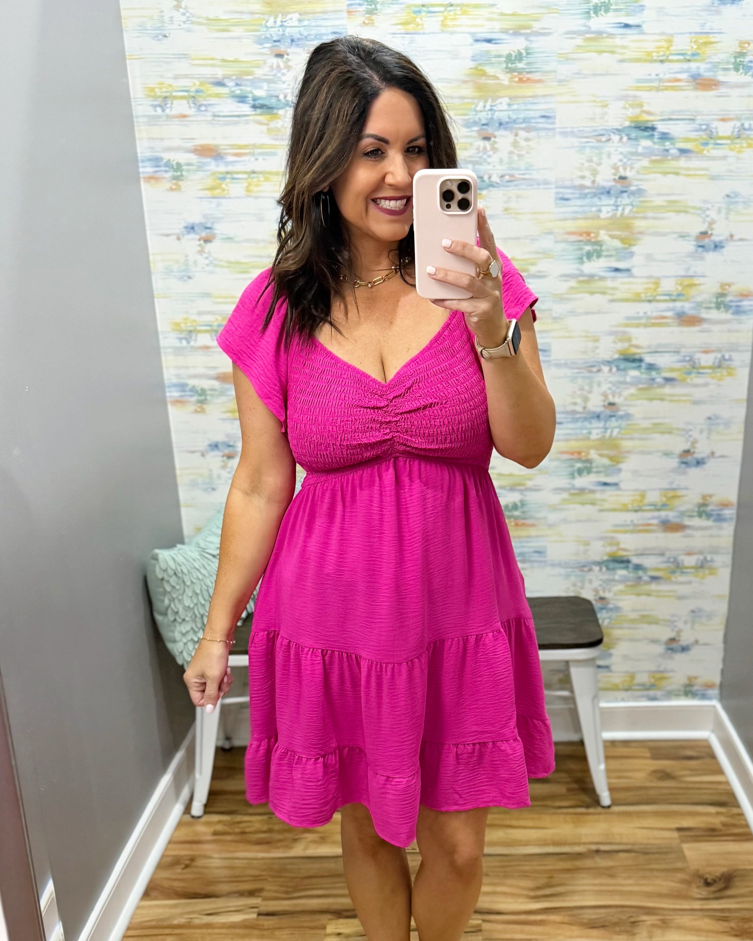 Woman wearing a pink dress taking a mirror selfie in a room with a colorful wall.