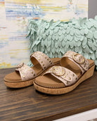 Pair of beige sandals with gold accents on a wooden surface with a decorative background.
