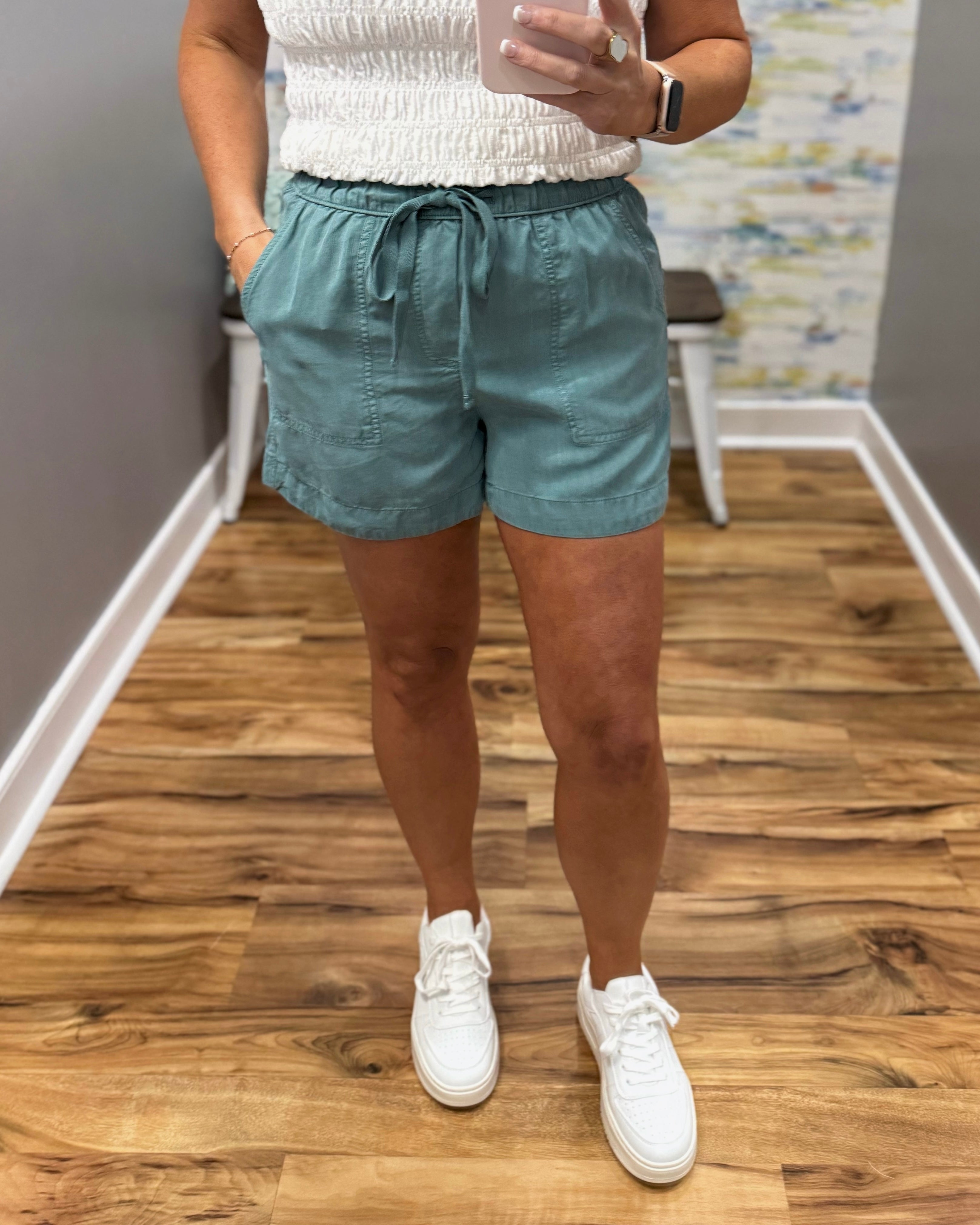 Person wearing light blue shorts and white sneakers on a wooden floor.
