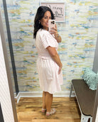 Woman taking a mirror selfie wearing a white dress in a room with colorful wallpaper.