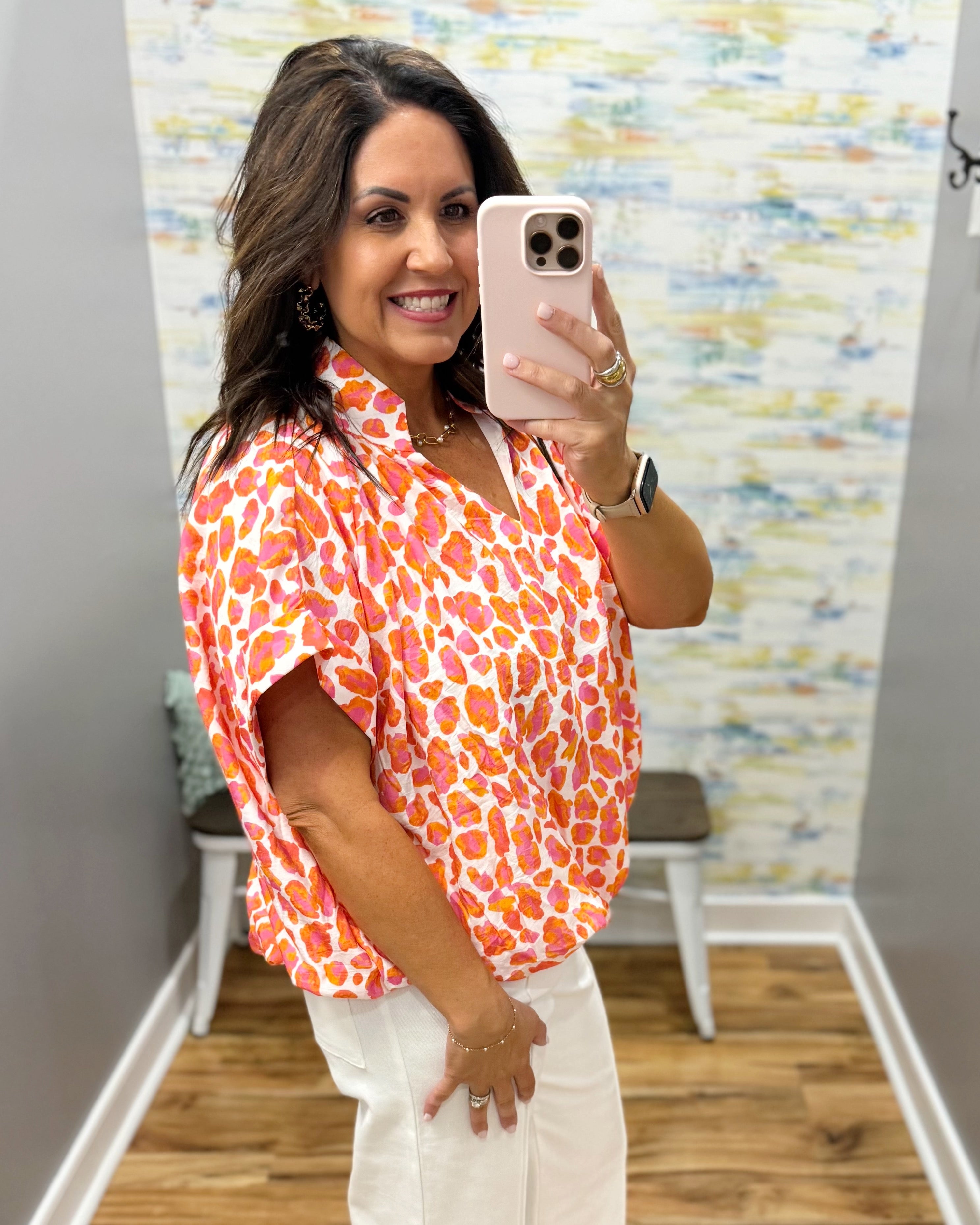Woman taking a mirror selfie wearing an orange and pink patterned shirt in a room with a colorful wall.