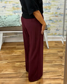 A woman takes a mirror selfie in a fitting room wearing a black short-sleeve sweater and high-waisted wide-leg pants in merlot with Corkys Sober Up shoes in leopard.