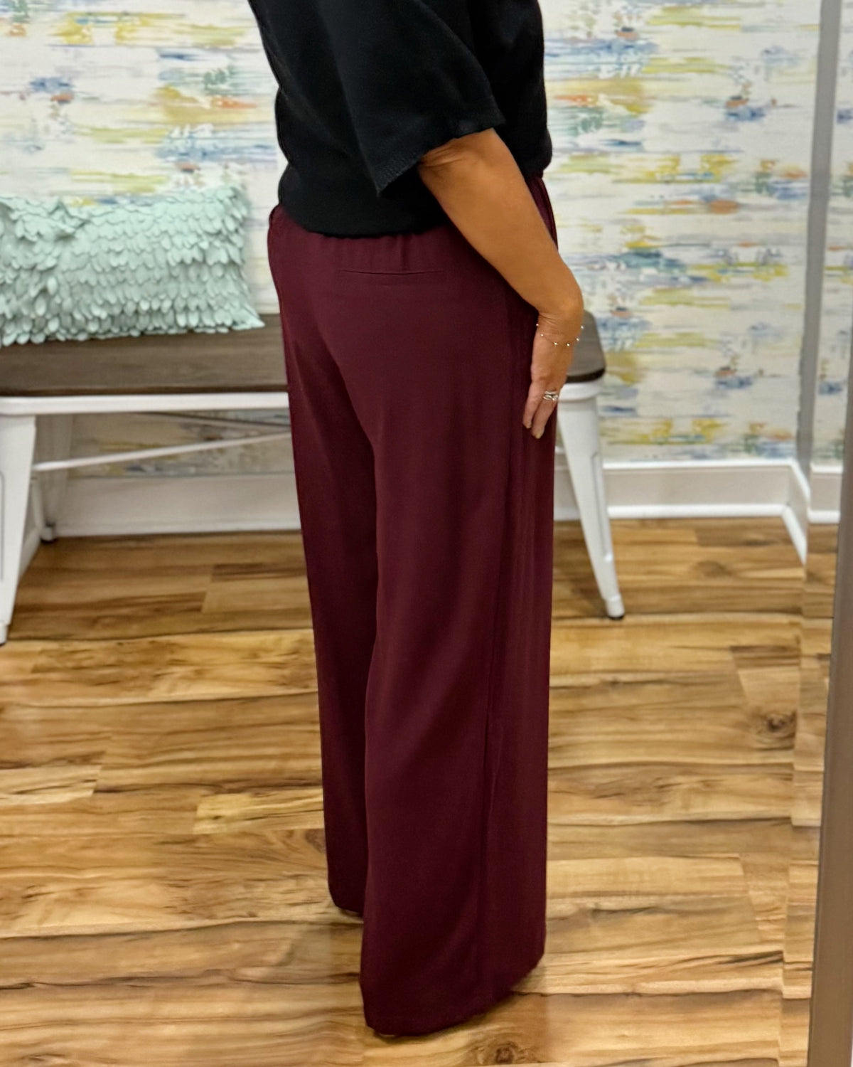 A woman takes a mirror selfie in a fitting room wearing a black short-sleeve sweater and high-waisted wide-leg pants in merlot with Corkys Sober Up shoes in leopard.