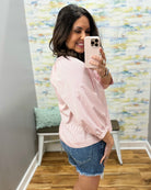Woman taking a mirror selfie wearing a pink striped shirt and denim shorts in a room with a colorful textured wall.