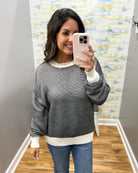A woman takes a mirror selfie wearing a gray and white horizontally striped knit sweater with white ribbed trim, paired with blue jeans.