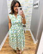 Woman taking a mirror selfie wearing a floral dress in a room with a colorful wall.