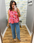 Woman taking a mirror selfie wearing a colorful top and blue jeans in a room with patterned wallpaper.