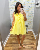 Woman taking a mirror selfie wearing a yellow dress in a room with a patterned wall.