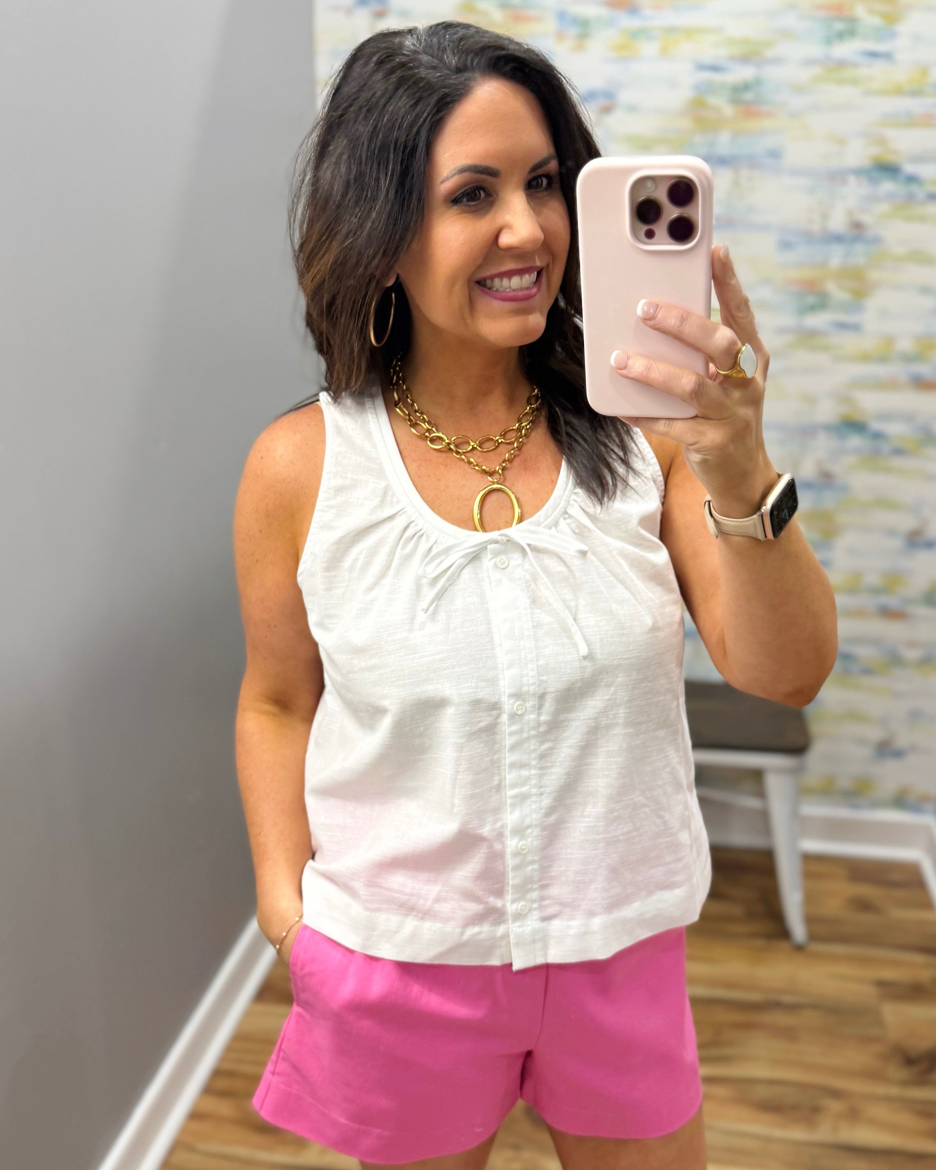 Woman wearing a white sleeveless top and pink shorts.