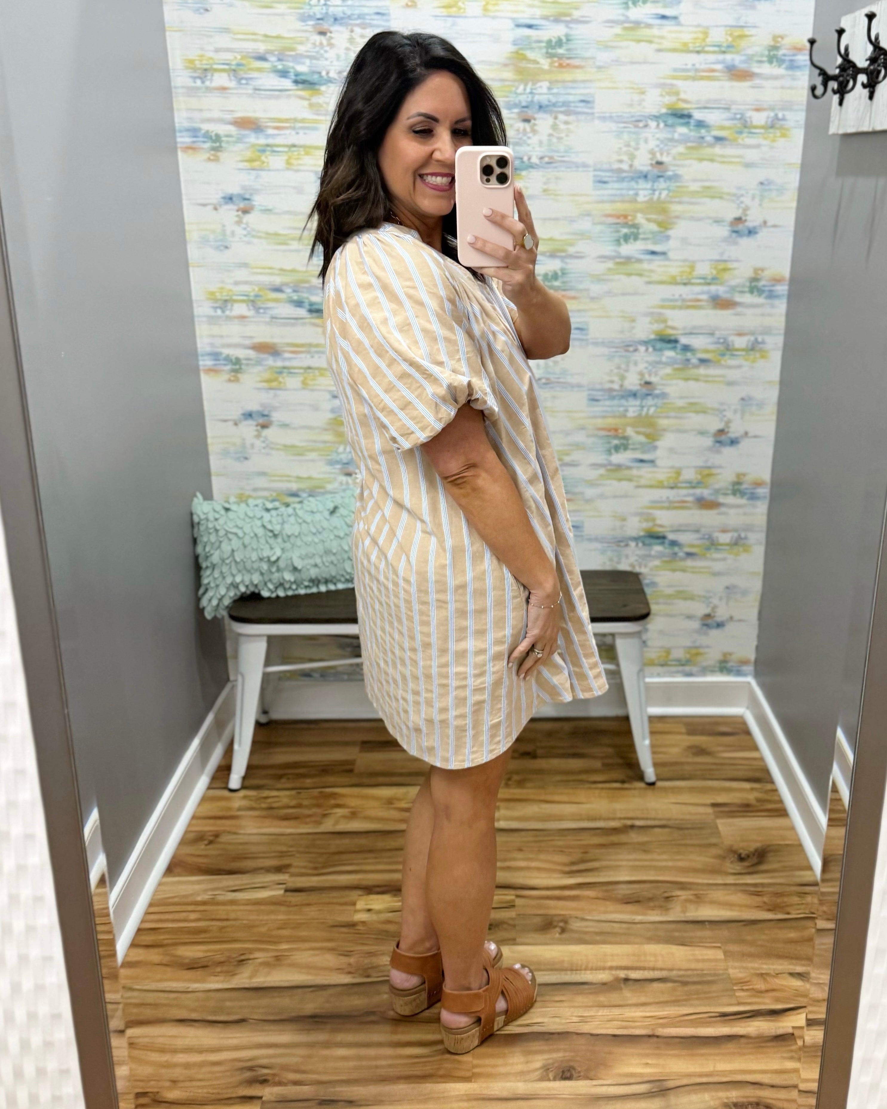 Woman taking a mirror selfie wearing a striped dress in a room with patterned wallpaper.