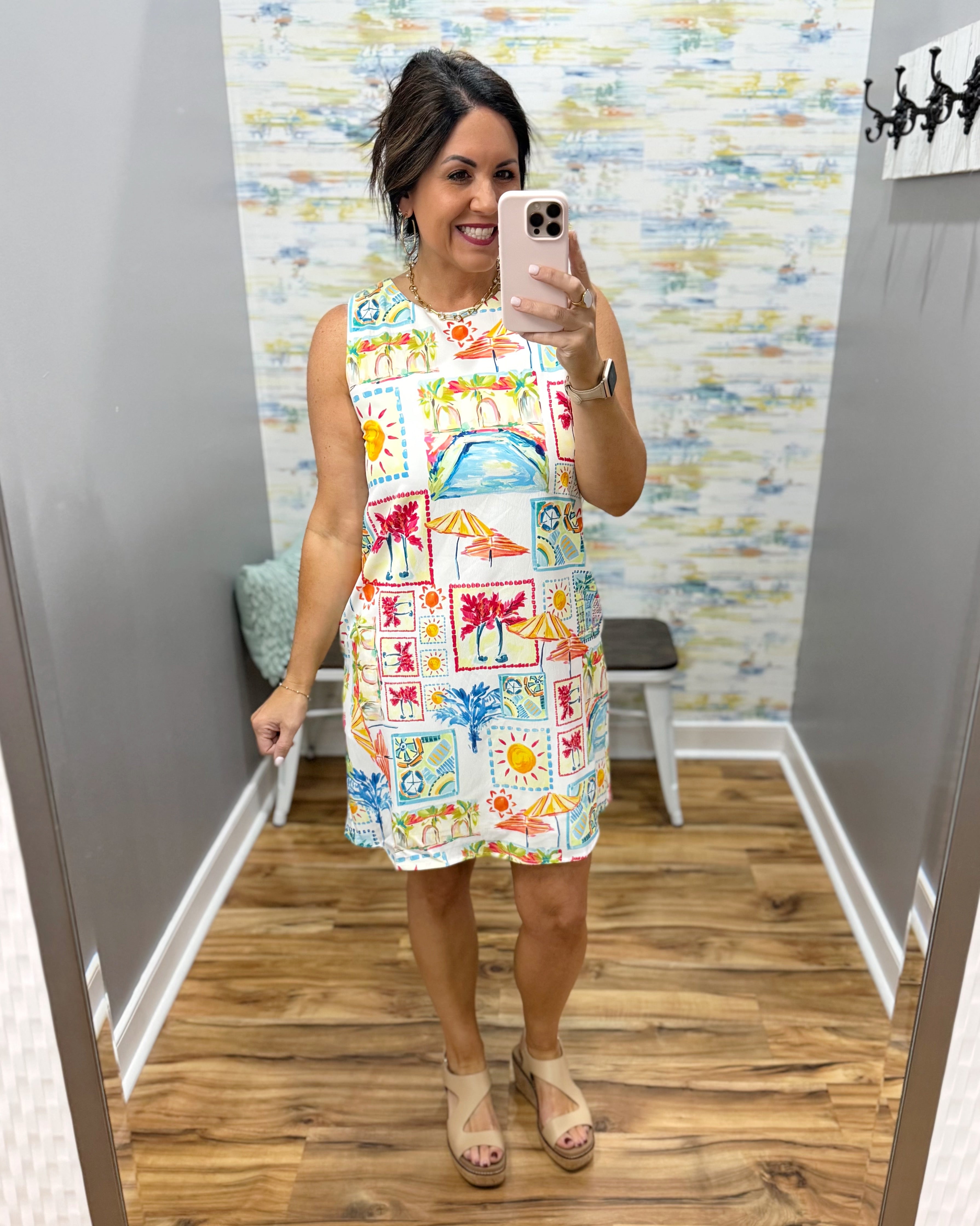 Woman taking a mirror selfie wearing a colorful patterned dress in a room with a patterned wall.