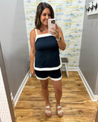 Woman taking a mirror selfie wearing a navy and white outfit in a room with wooden flooring and colorful wall.