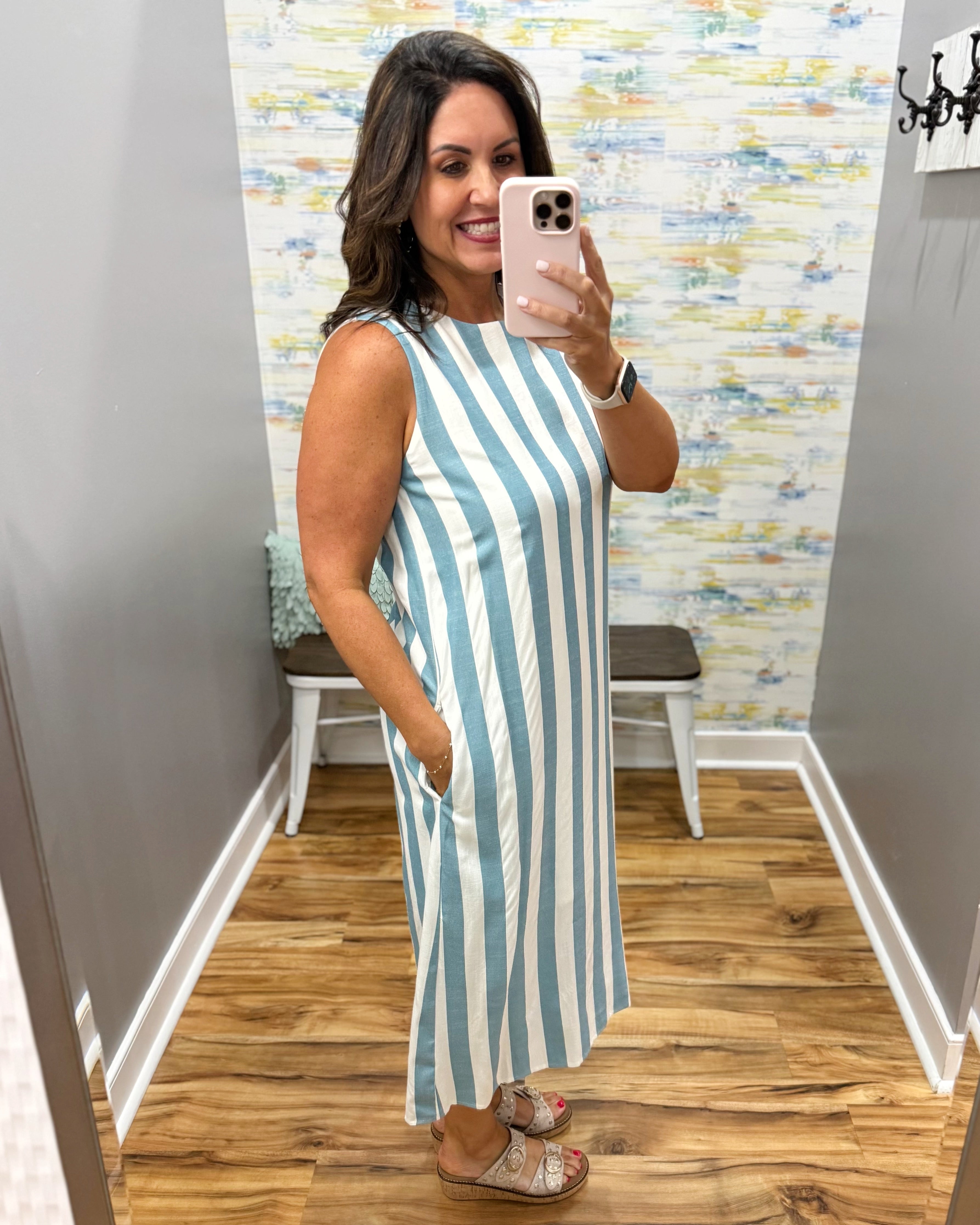 Woman taking a mirror selfie wearing a blue and white striped dress in a room with a patterned wall.