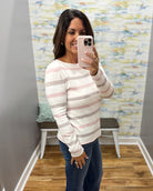 A woman takes a mirror selfie wearing a long-sleeve knit sweater with horizontal stripes in white, light pink, and taupe, paired with dark blue jeans.