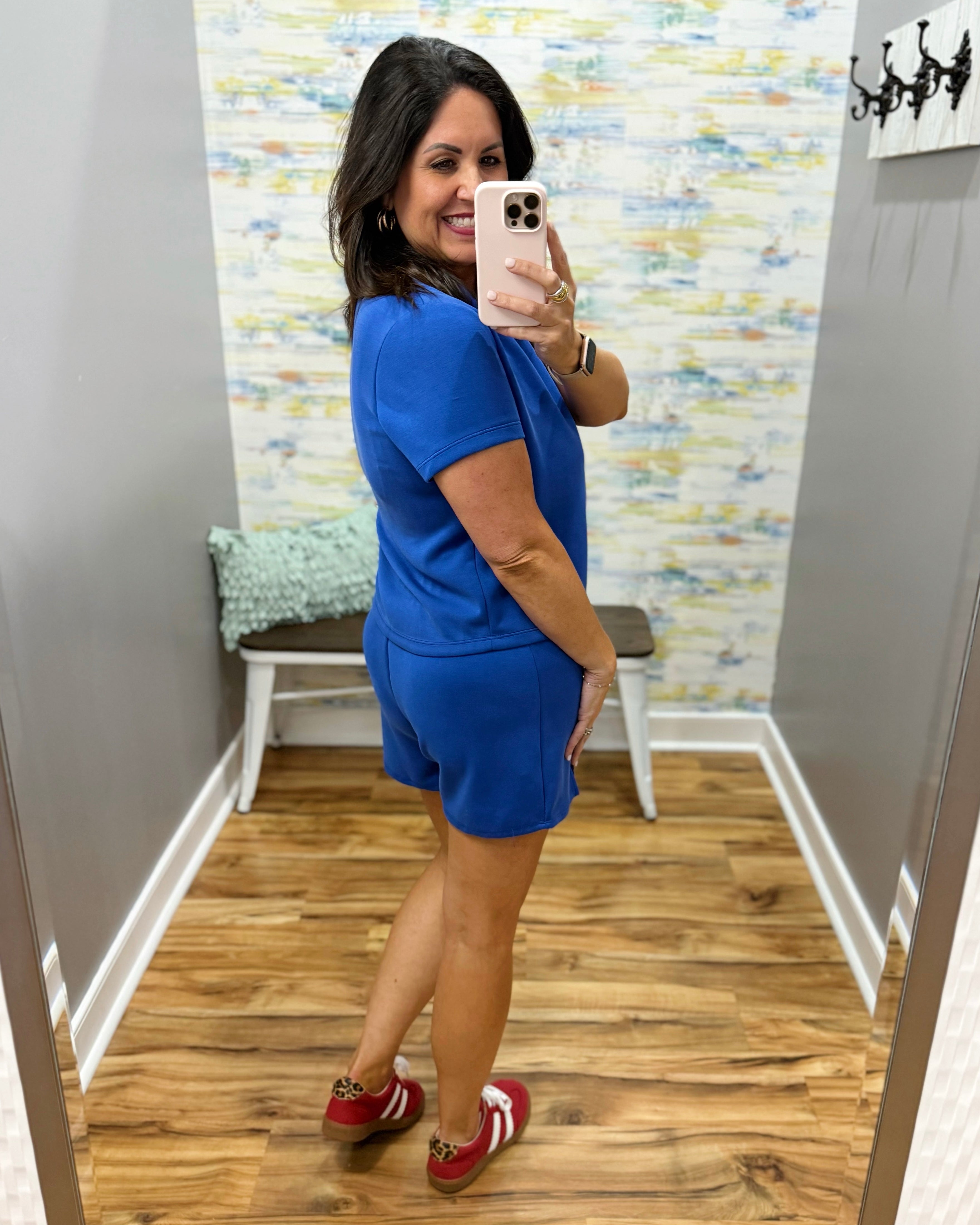 Woman taking a mirror selfie wearing a blue outfit in a room with a colorful wall.