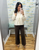 A woman takes a mirror selfie in a fitting room wearing a cream-colored textured knit zip-up cardigan, dark brown wide-leg pants, and leopard print pointed flats.