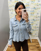 A woman taking a mirror selfie in a boutique wearing a light-wash blue denim jacket and dark brown pants.