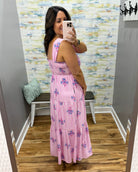 Woman taking a mirror selfie wearing a pink dress with a floral pattern in a room with a textured wall.