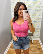 Woman taking a mirror selfie wearing a pink tank top and denim shorts in a room with a colorful wall.