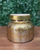 Gold-speckled candle jar with a gold lid on a wooden surface with a green blurred background