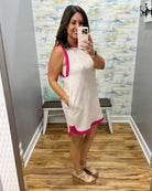Woman taking a mirror selfie wearing a dress with pink trim in a room with a patterned wall.