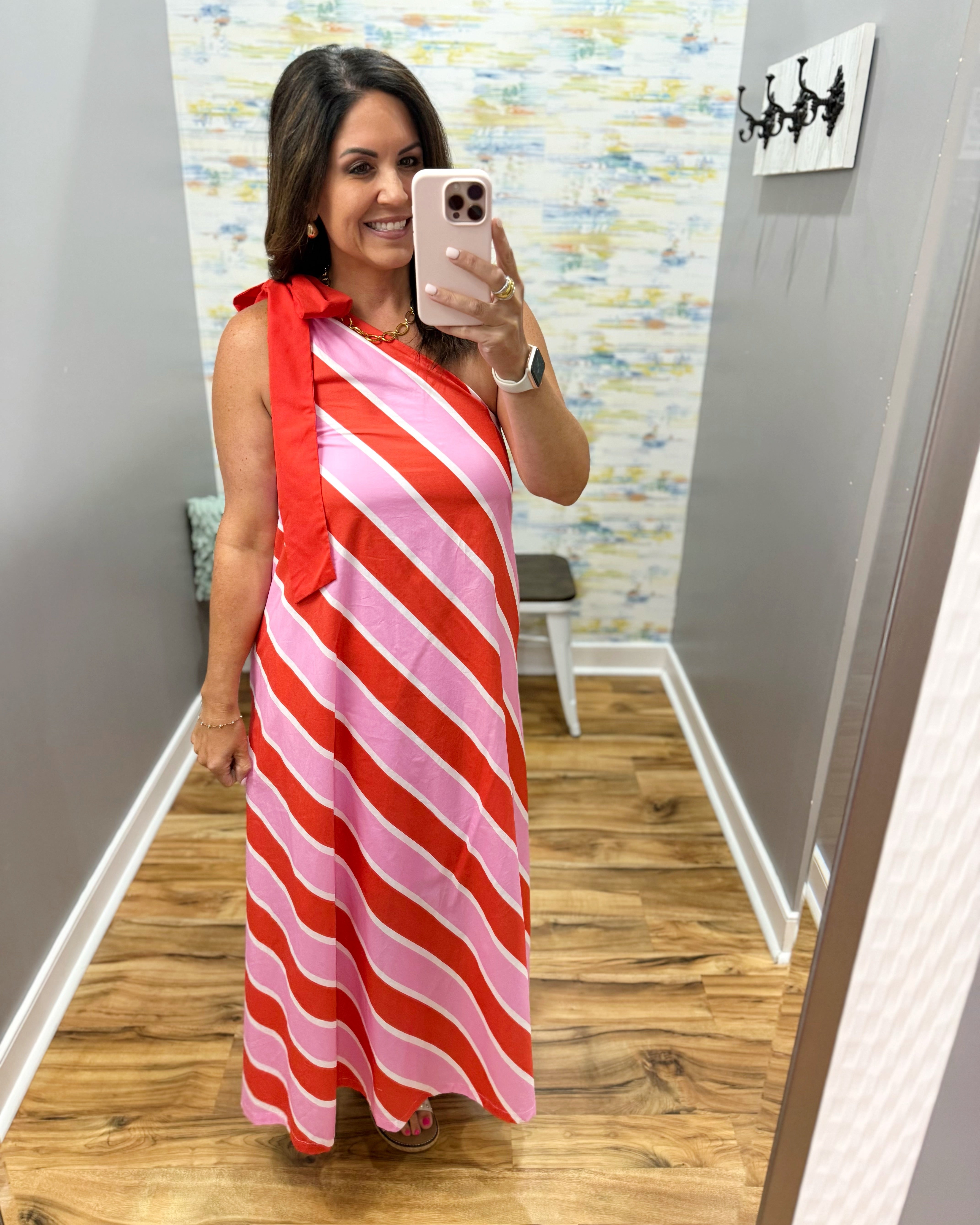 Woman taking a mirror selfie wearing a red and pink striped dress.