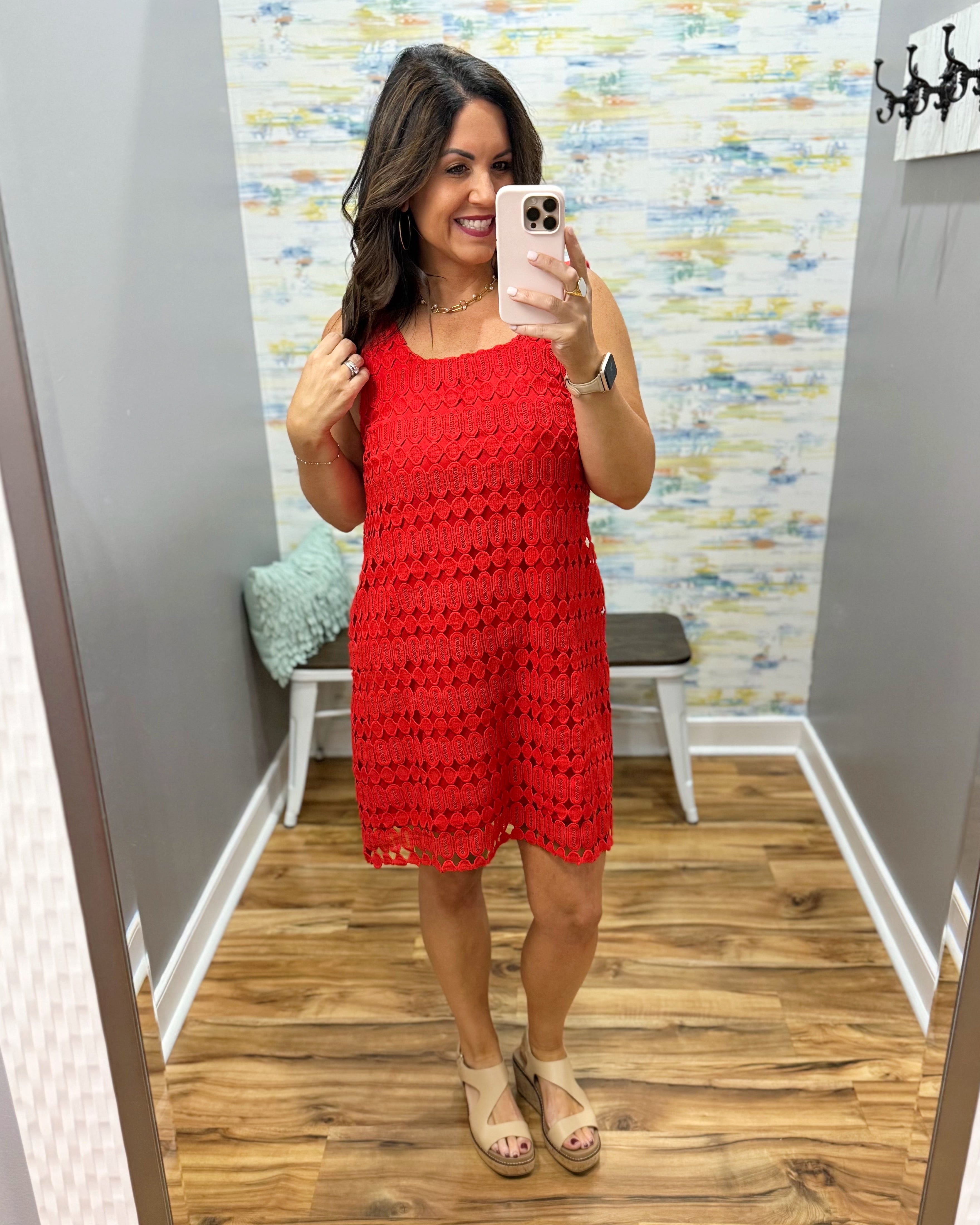 Woman taking a mirror selfie wearing a red dress in a room with a colorful wall.