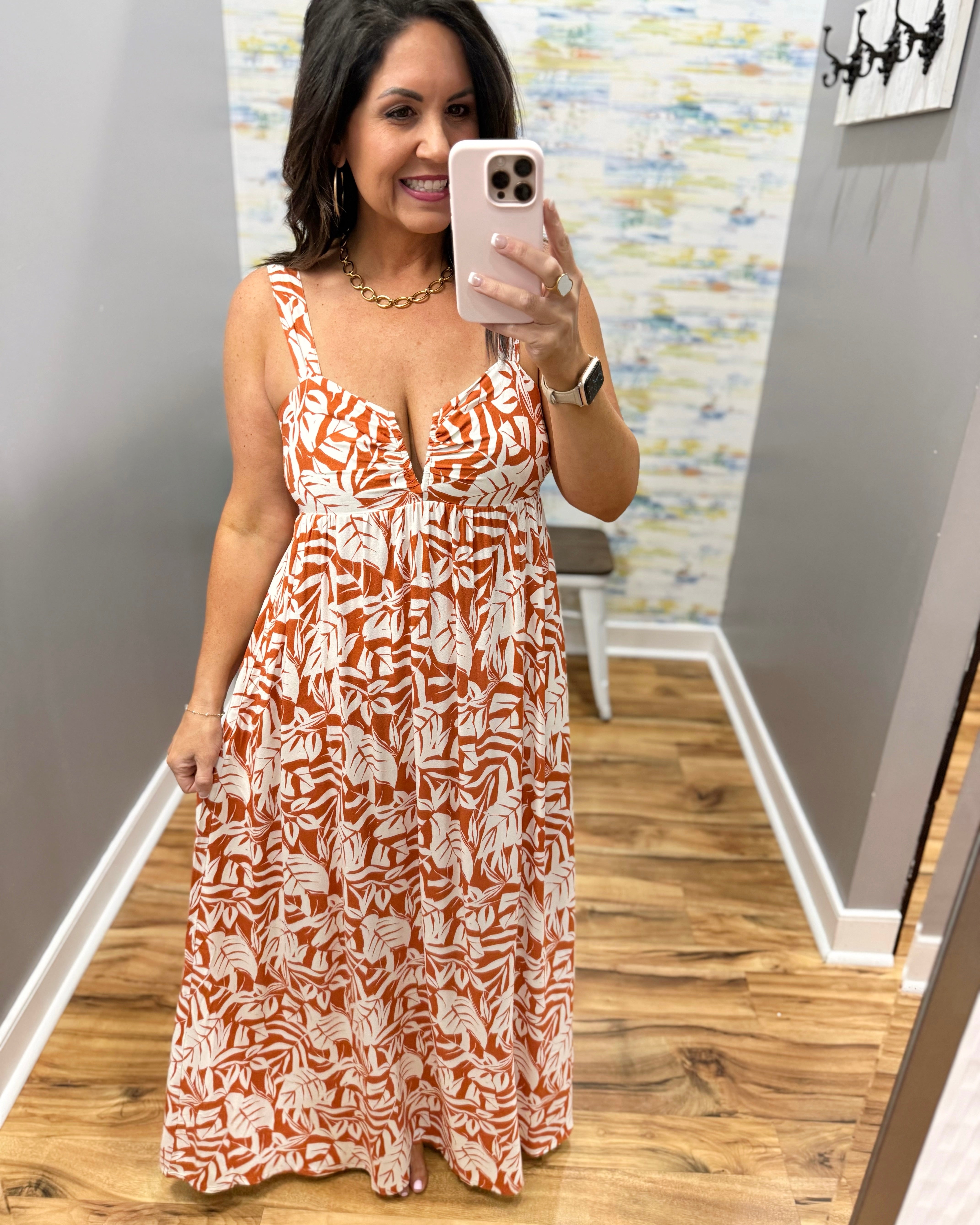 Woman taking a mirror selfie wearing a patterned dress in a room with a colorful wall.