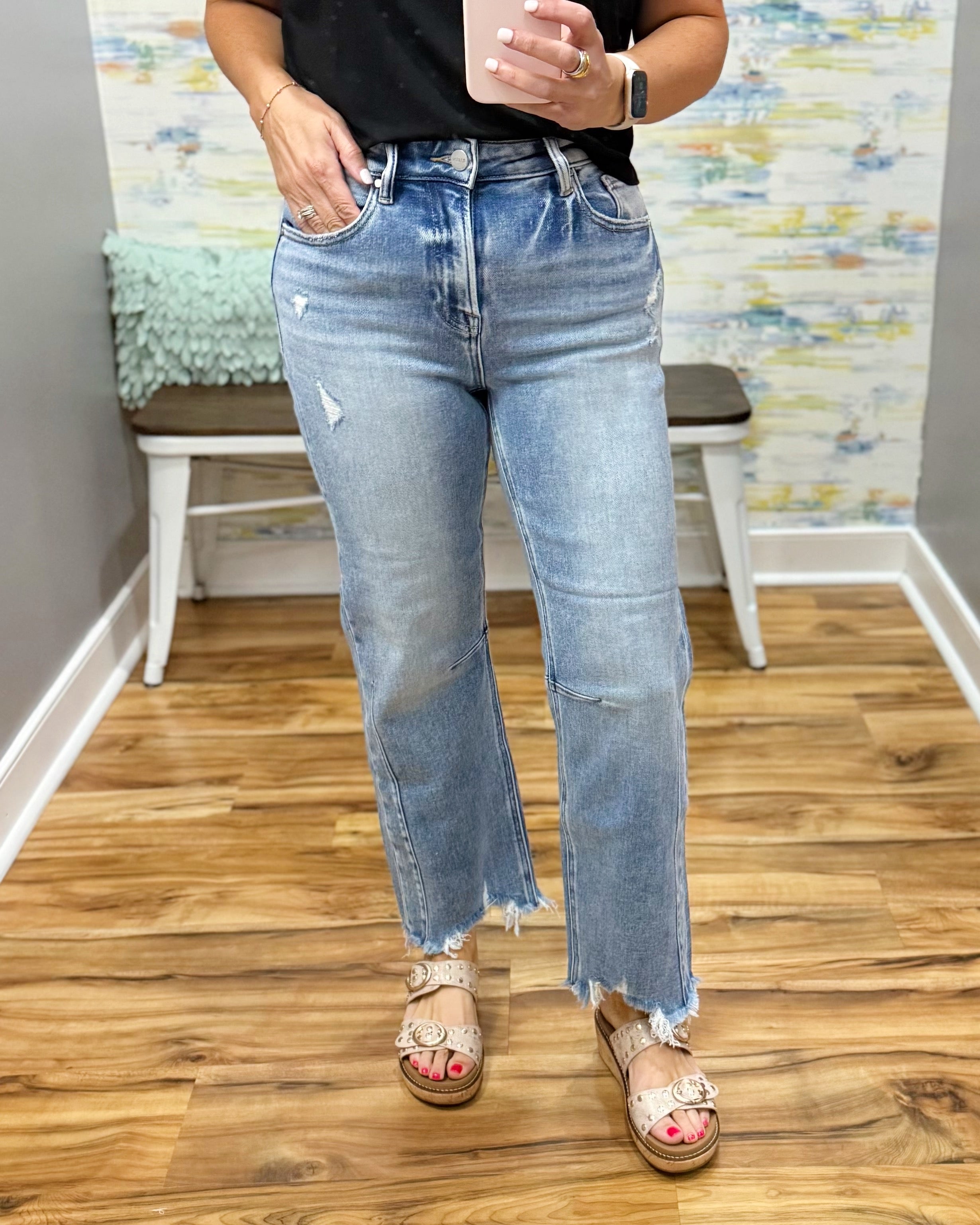 Person wearing light blue jeans standing on a wooden floor with a colorful wall in the background.