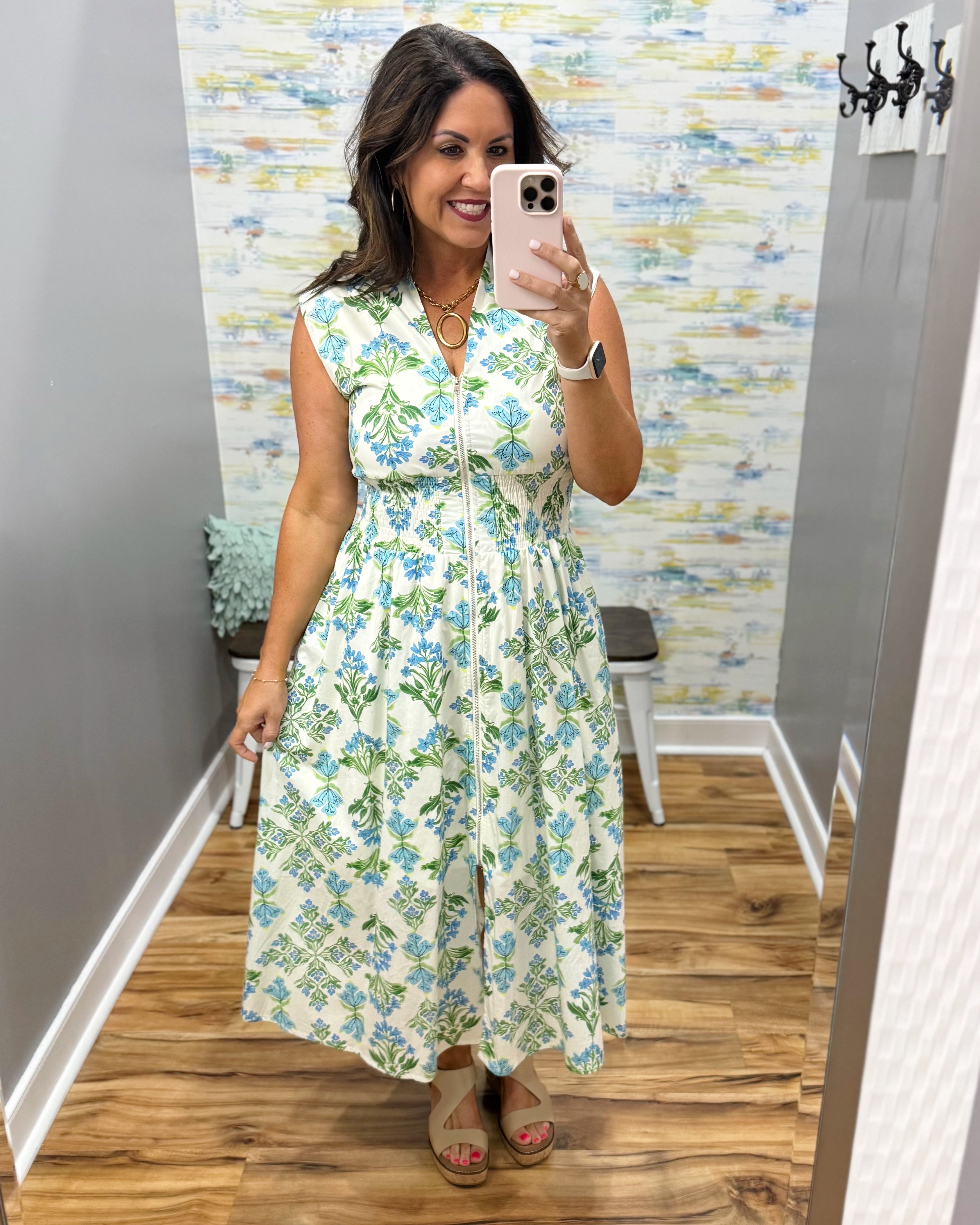 Woman taking a mirror selfie wearing a floral dress in a room with a patterned wall.