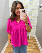 Woman taking a mirror selfie wearing a bright pink top and blue jeans.