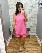 Woman taking a mirror selfie wearing a pink dress in a room with patterned wallpaper.