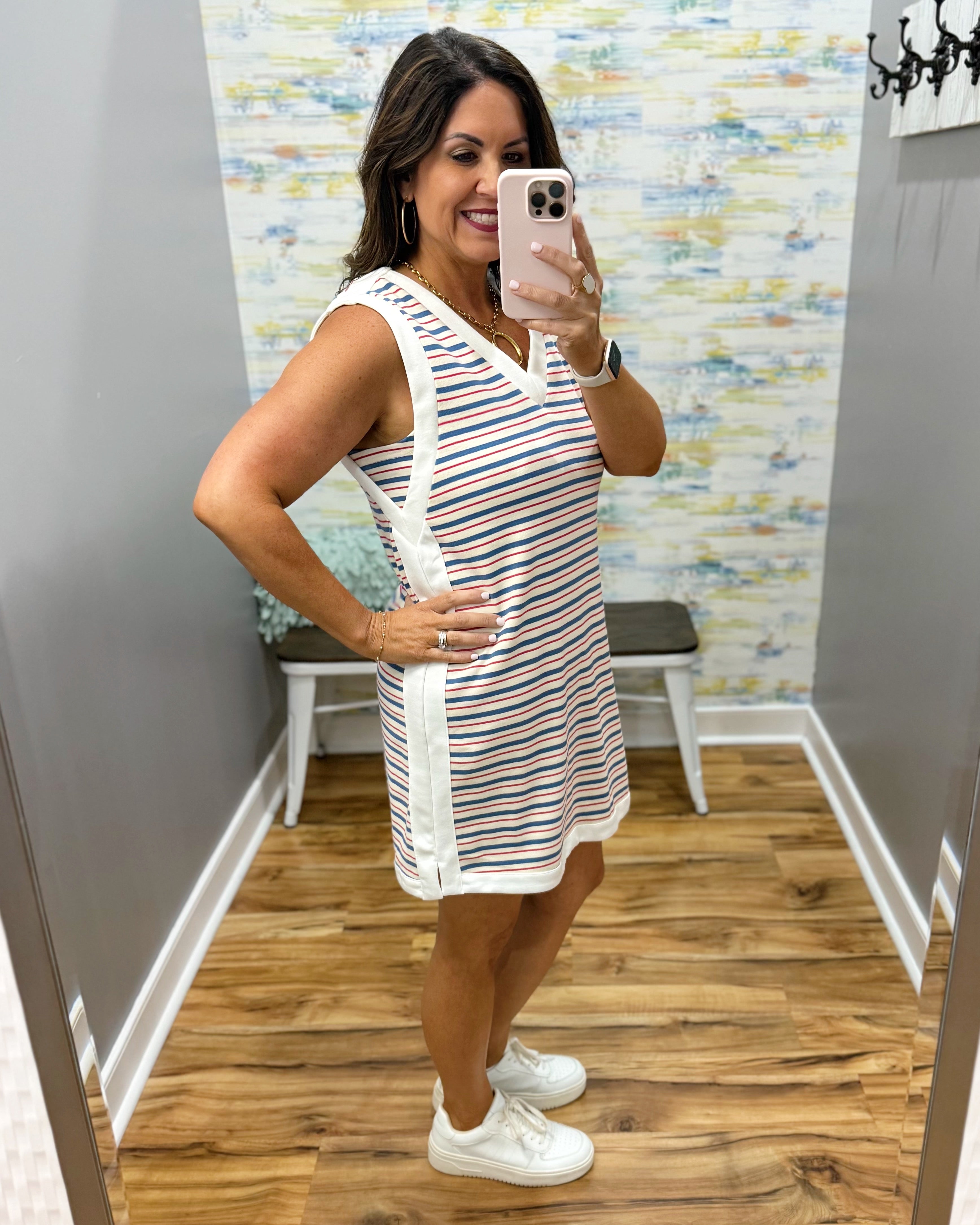 Woman taking a mirror selfie wearing a striped dress in a fitting room.