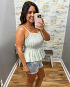Woman taking a mirror selfie wearing a striped peplum top and denim shorts in a room with a colorful wall.