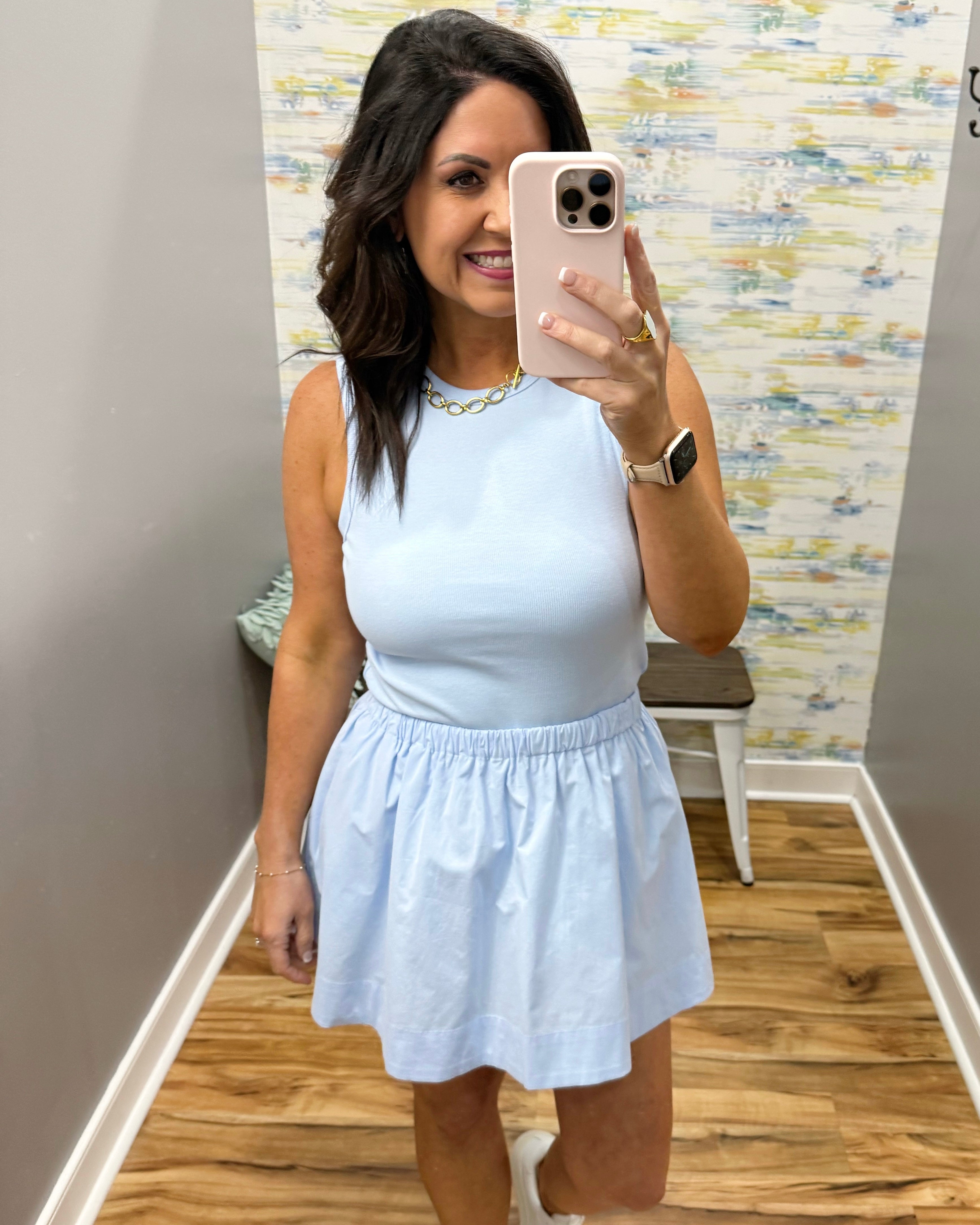 Woman taking a mirror selfie wearing a light blue dress in a room with a patterned wall.