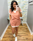 Woman taking a mirror selfie wearing a pink outfit in a room with wooden flooring and a colorful wall.