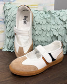 Pair of children's shoes with a strap on a wooden surface with a textured green fabric background.