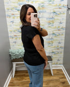 Woman taking a mirror selfie wearing a black top and blue jeans in a room with colorful wall art.