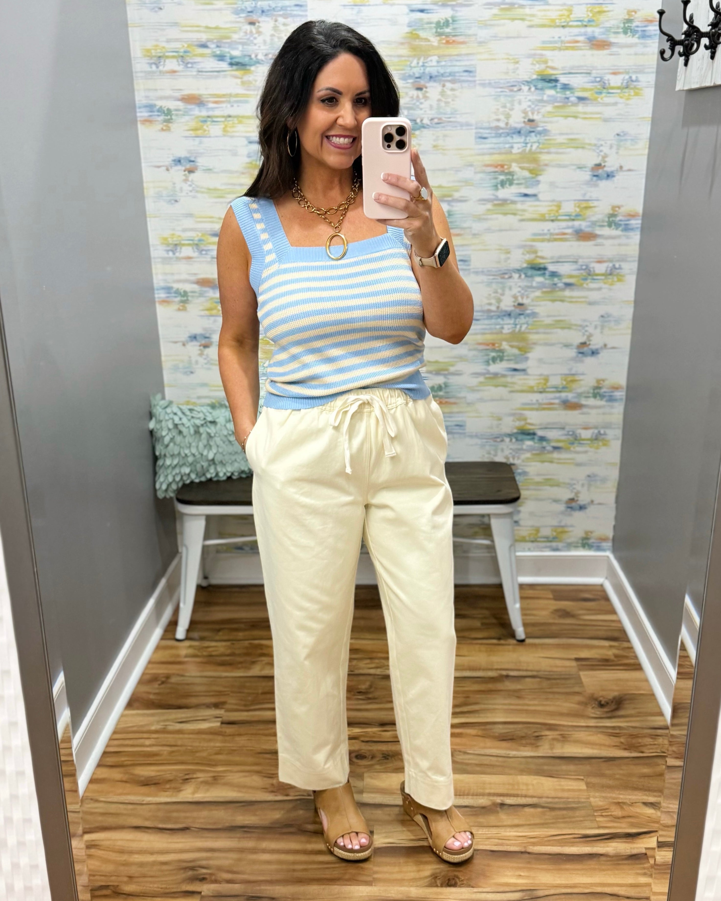 Woman wearing a striped top and beige pants in a room with a textured wall.