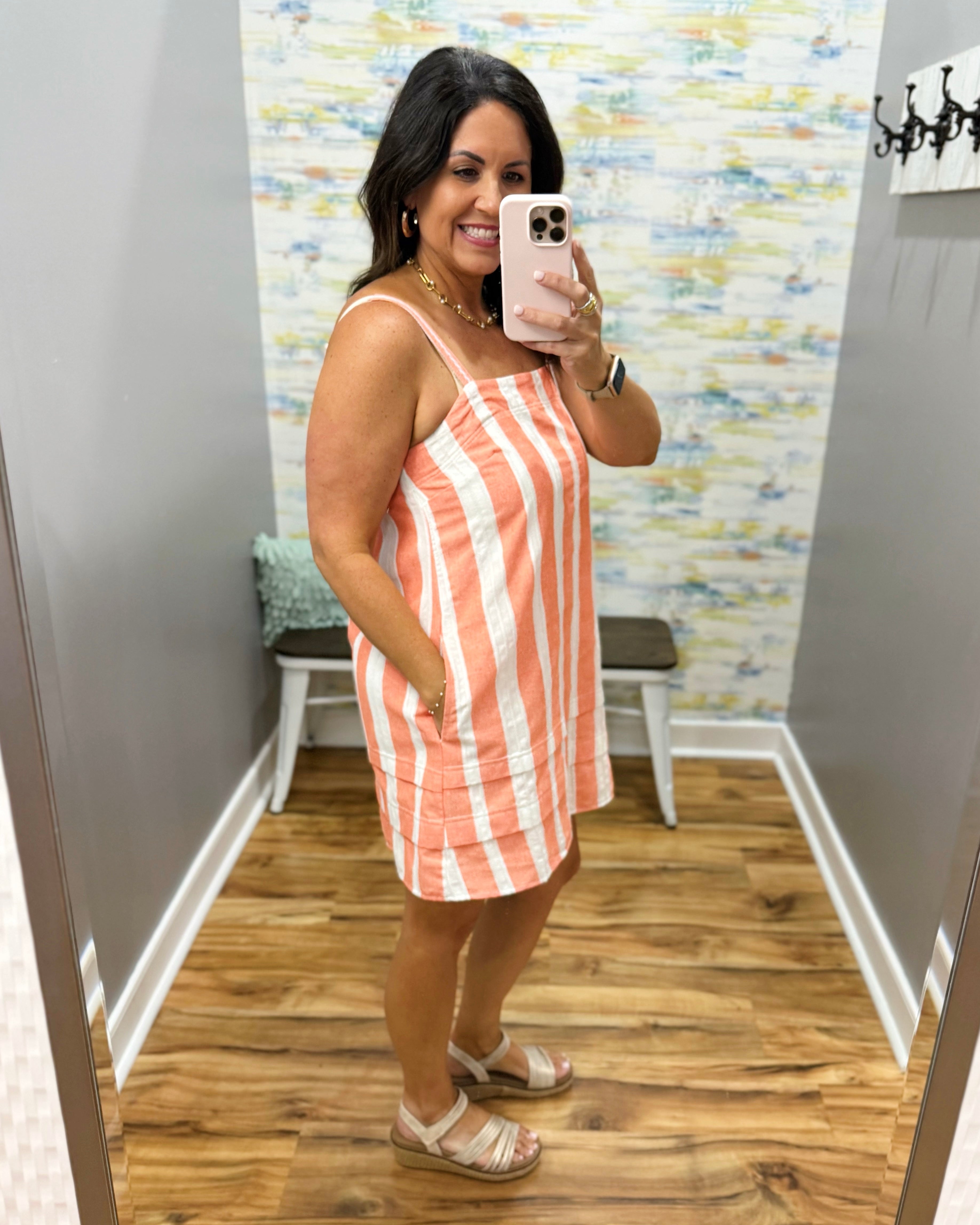 Woman taking a mirror selfie wearing a striped dress in a room with colorful wall art.