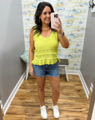 Woman taking a mirror selfie wearing a yellow top and denim shorts in a room with patterned wallpaper.