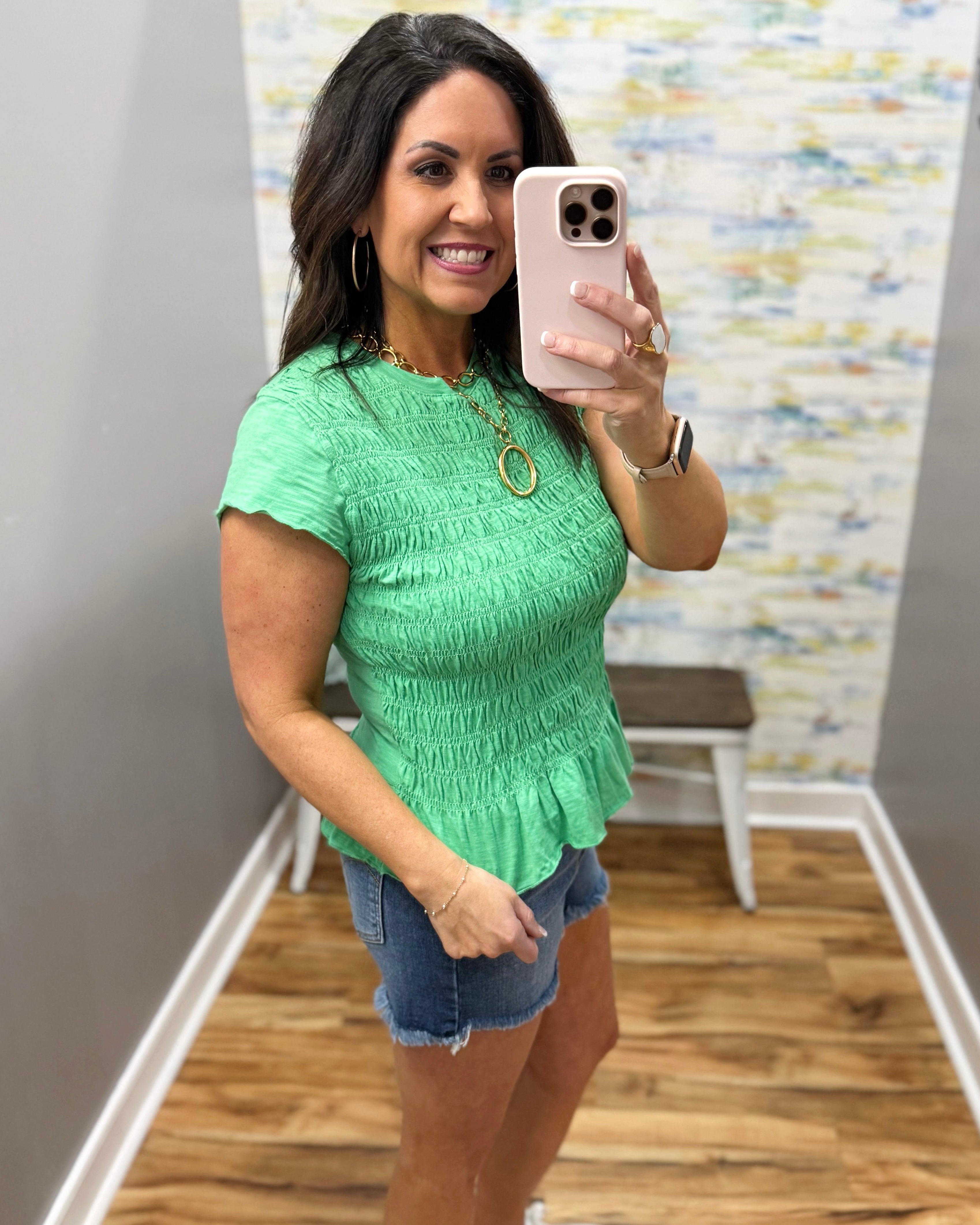 Woman wearing a green top and denim shorts in a room with a textured wall.