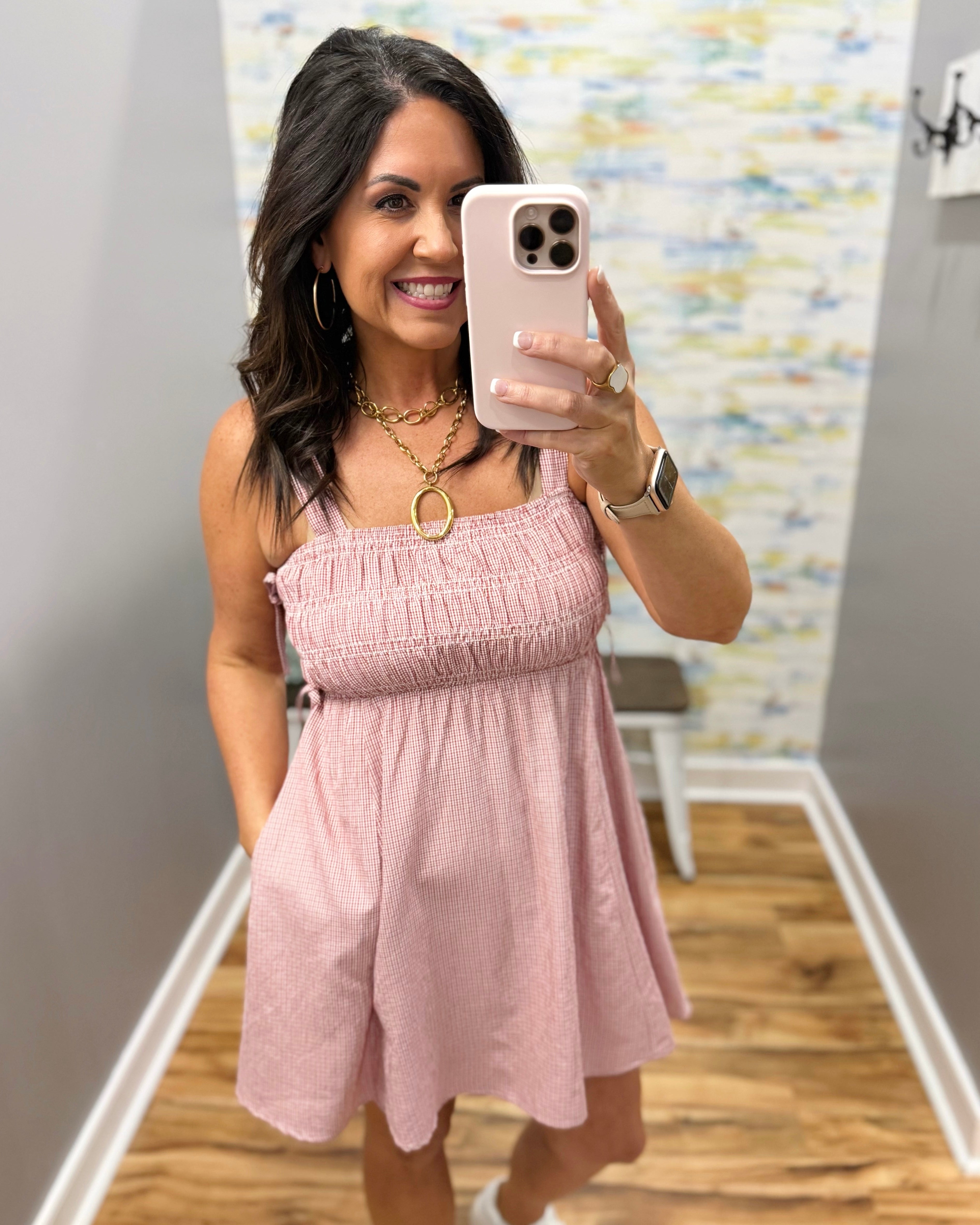 Woman taking a mirror selfie wearing a pink dress in a room with a colorful wall.
