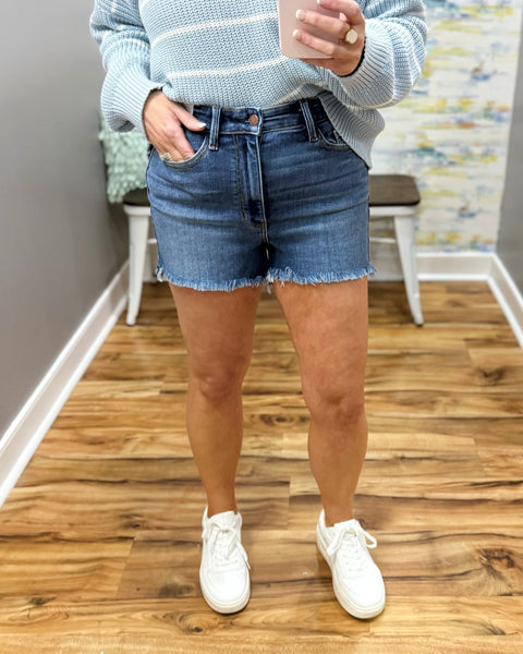 Person wearing denim shorts and a light gray sweater on a wooden floor.