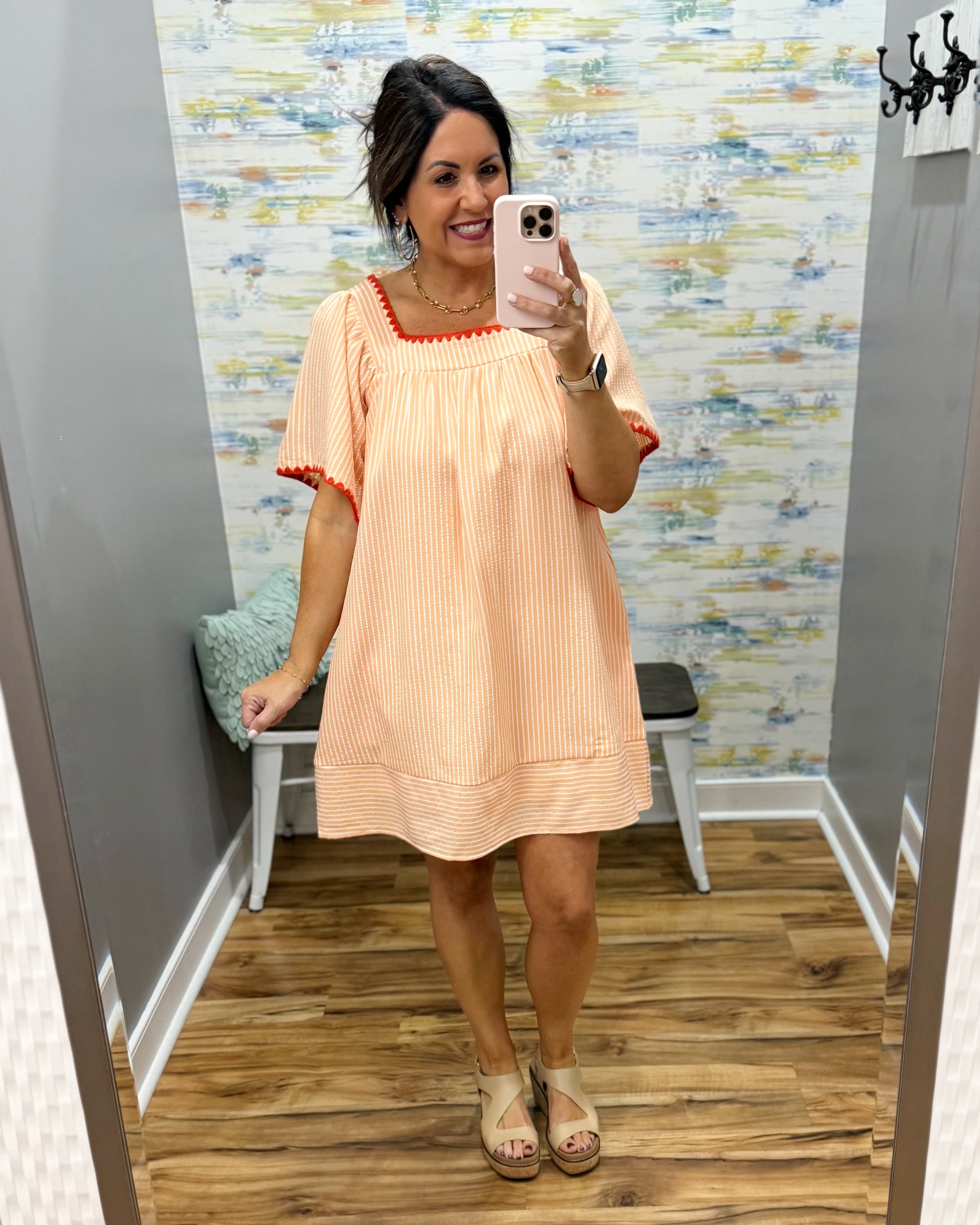 Woman taking a mirror selfie wearing a peach dress with red trim in a fitting room.